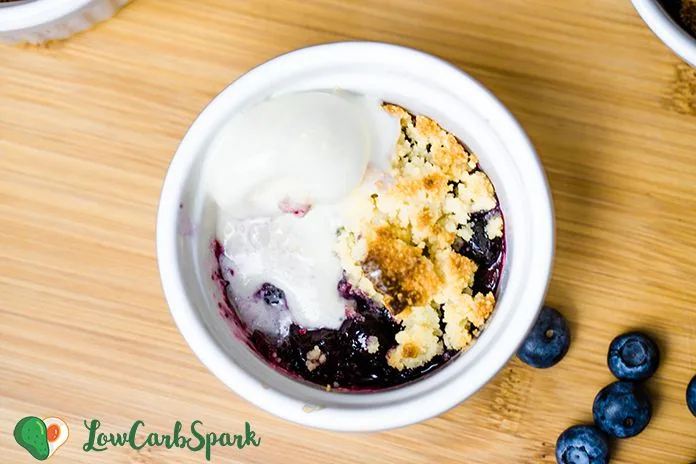 The Best Buttery Keto Blueberry Cobbler 4 Low carb blueberry cobbler in a white ramekin with juicy baked blueberries and buttery crumble topping