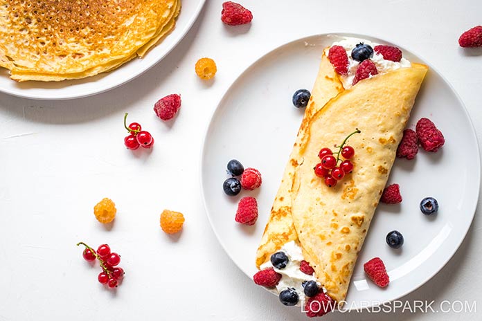 Keto Crepes on a white background served with whipped cream and fresh berries