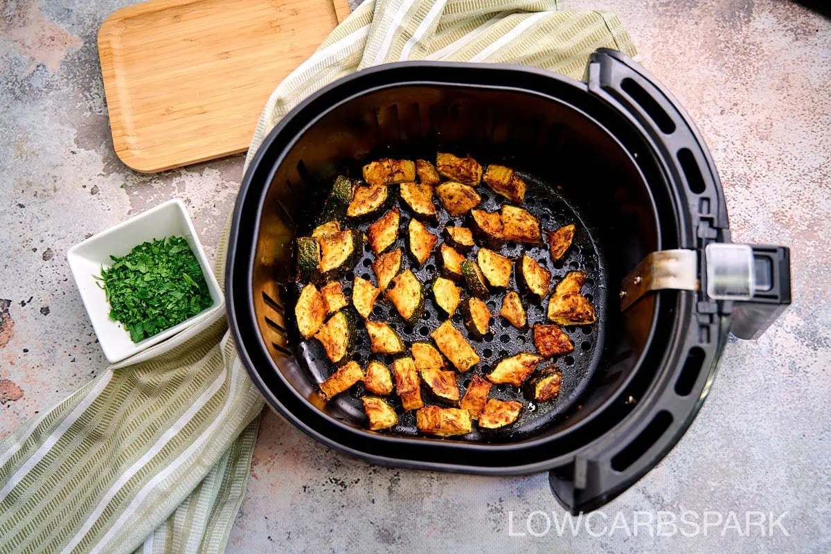 Air Fryer Zucchini 5 Overhead view of seasoned zucchini slices arranged in a single layer inside an air fryer basket, golden and crisp around the edges.