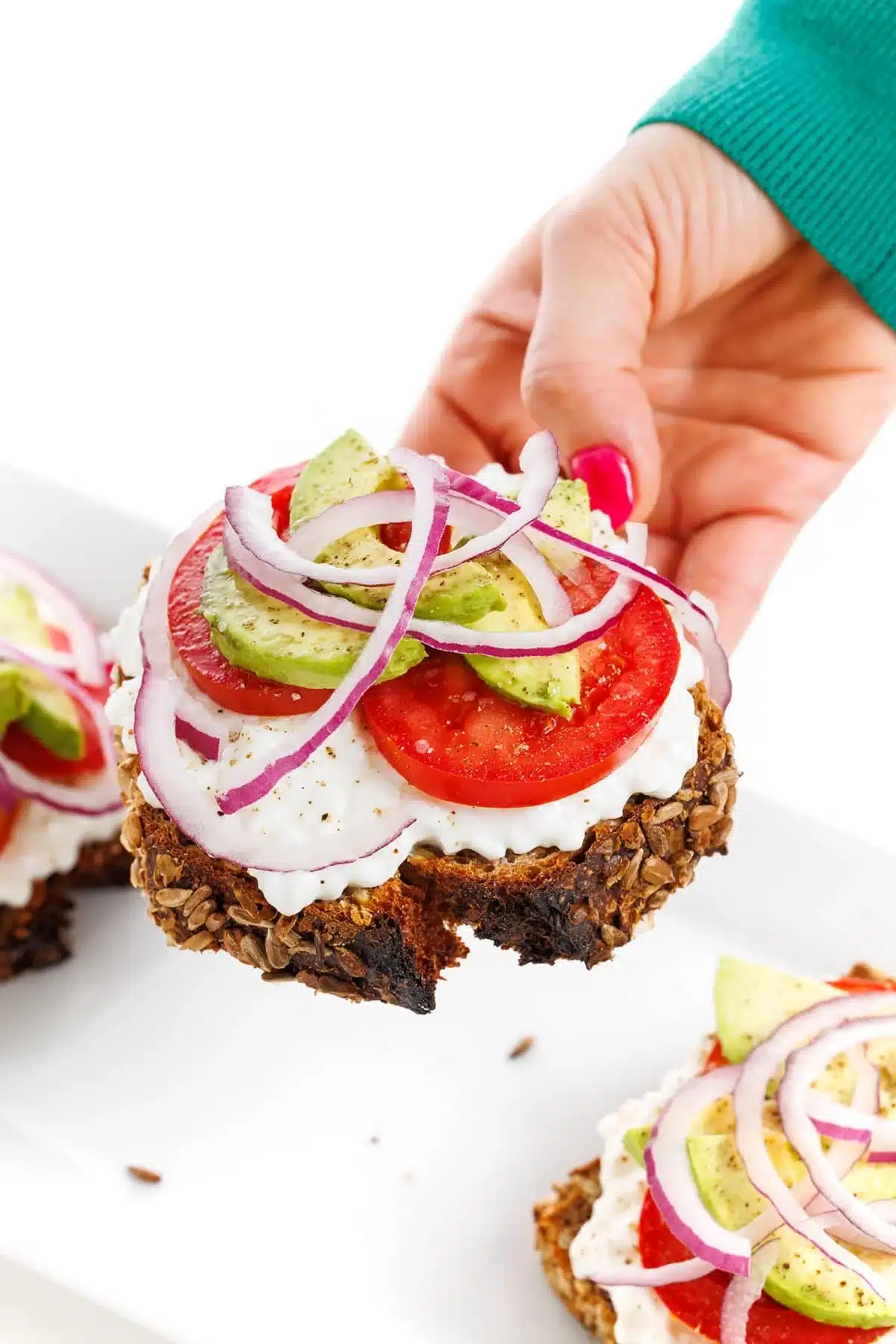 Holding avocado toast with cottage cheese and tomatoes