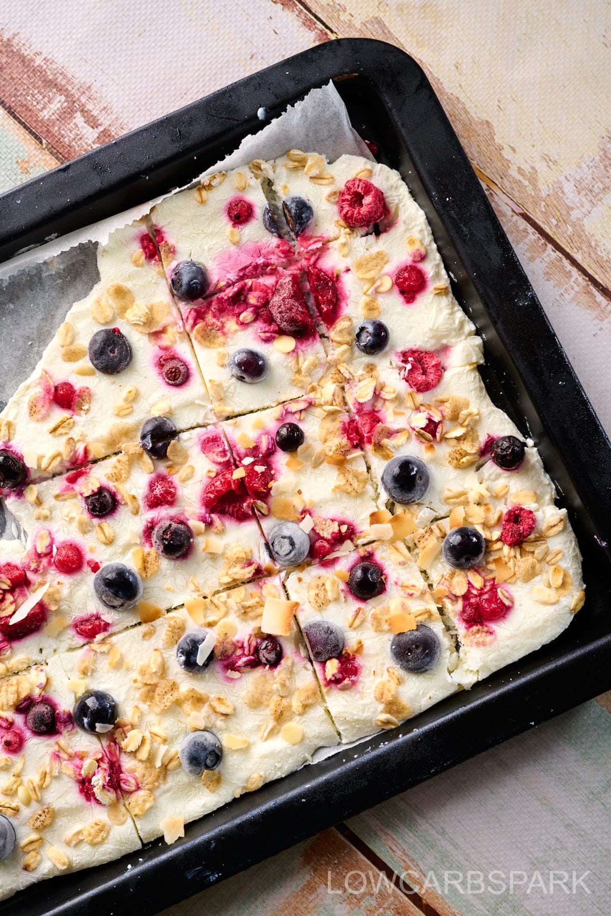 Baking sheet filled with Greek yogurt topped with blueberries, raspberries, and granola, ready for freezing.