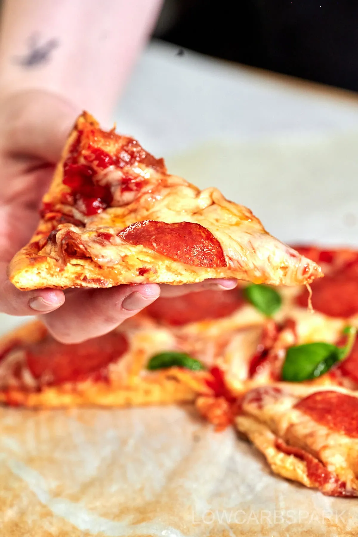 Cottage Cheese Pizza Crust 4 Keto pizza slice topped with basil and pepperoni held over pizza tray.