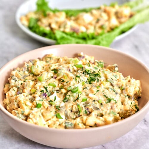 A creamy bowl of cottage cheese egg salad garnished with herbs in a soft pink bowl on a marble countertop.