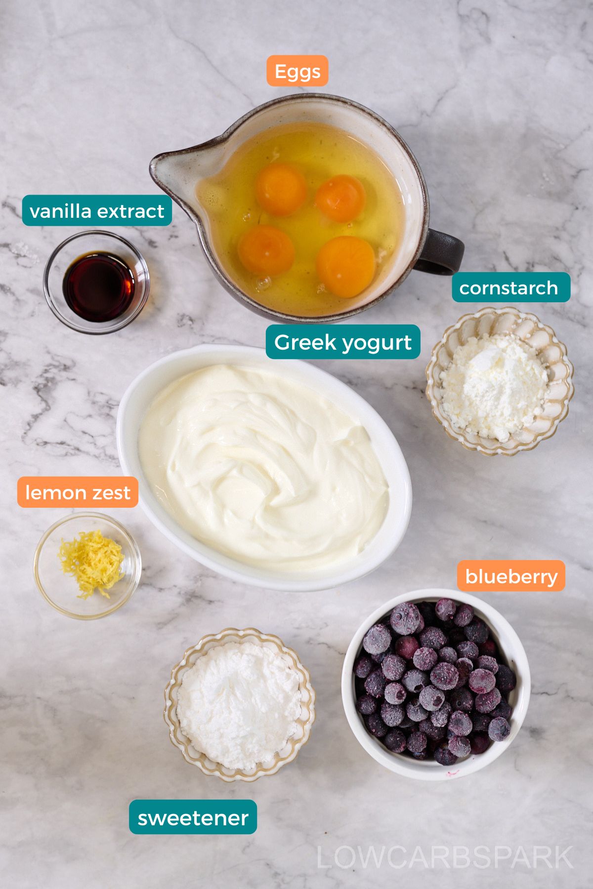 Ingredients laid out on marble counter with text labels such as lemon zest, vanilla extract, and cornstarch.