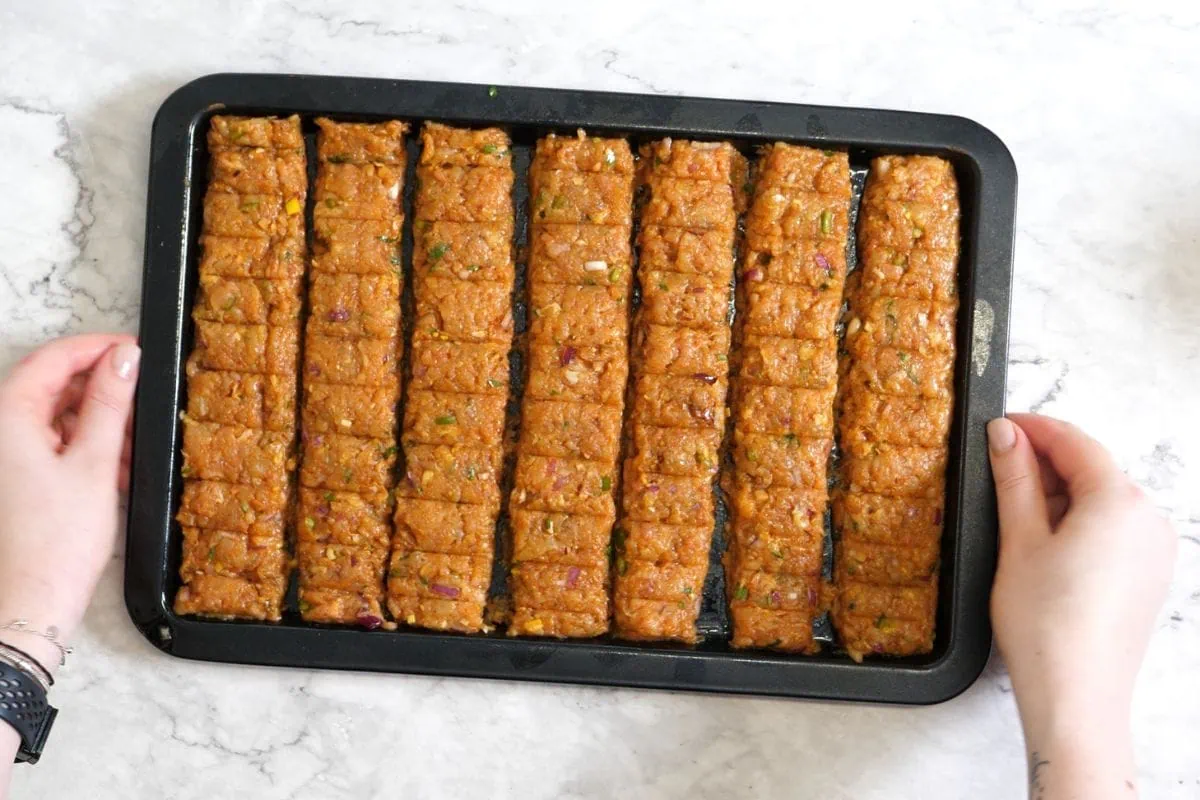 Sheet Pan Ground Chicken Kebabs 8 Neatly portioned chicken kebabs on a baking pan, ready to bake.