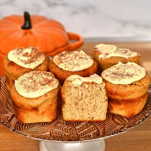 Cottage Cheese Pumpkin Muffins 4 High-protein cottage cheese pumpkin muffins with cream cheese frosting displayed on a cake stand.