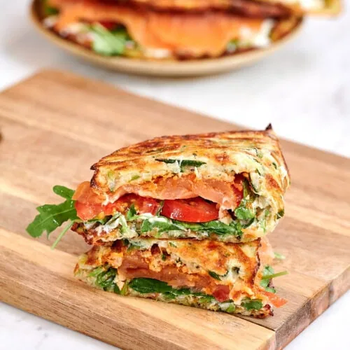 Zucchini Wraps 11 Stack of zucchini wraps filled with smoked salmon, arugula, and tomatoes on a wooden board.