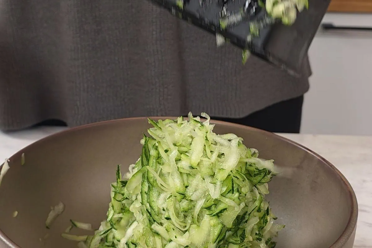 Zucchini Wraps 4 Step of preparing zucchini base by grating fresh zucchini into a bowl.