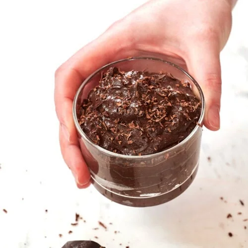 Boiled Egg Chocolate Mousse 9 Hand holding a glass of rich boiled egg chocolate mousse topped with shaved dark chocolate.