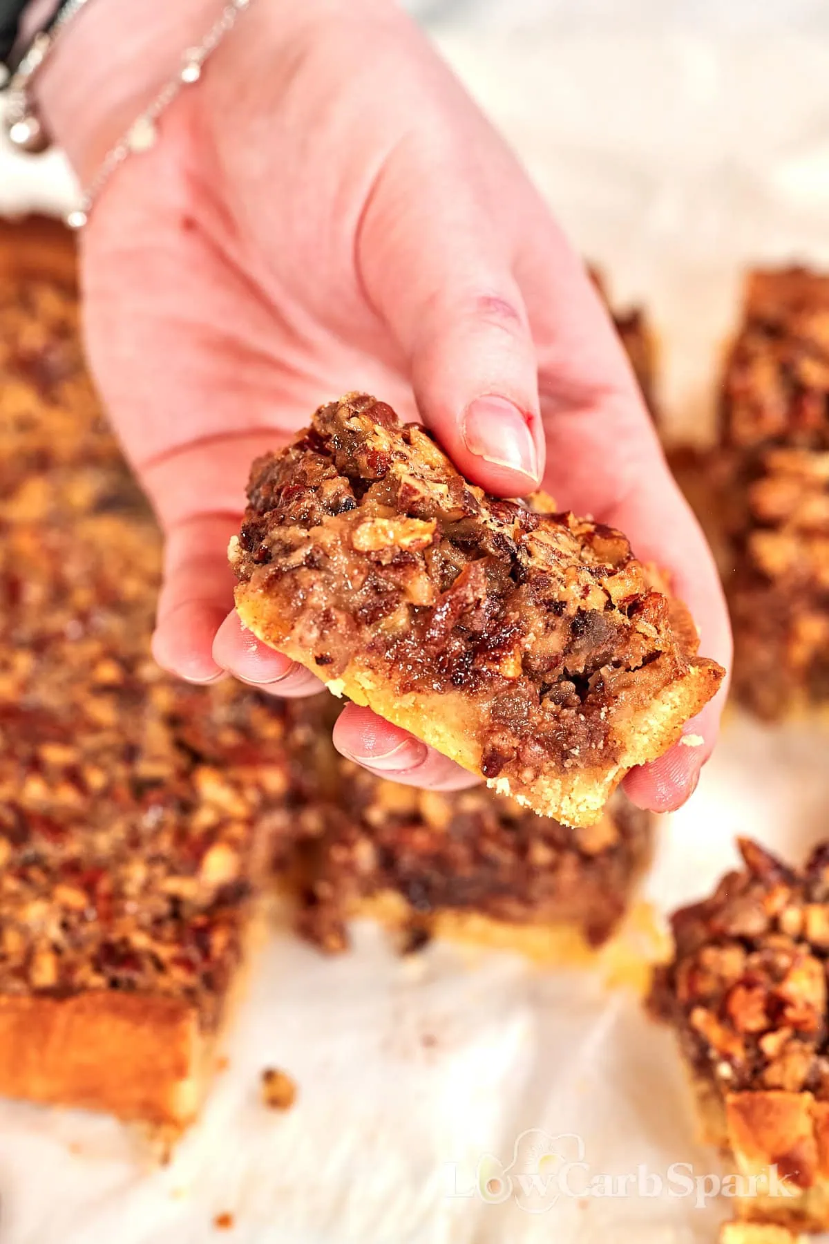 Keto Pecan Pie Bars 1 Keto pecan pie bar lifted from the pan, showing the pecan filling and almond flour crust