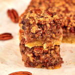 Stacked keto pecan pie bars with whole pecans scattered around them