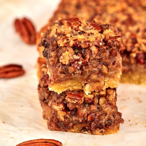 Stacked keto pecan pie bars with whole pecans scattered around them