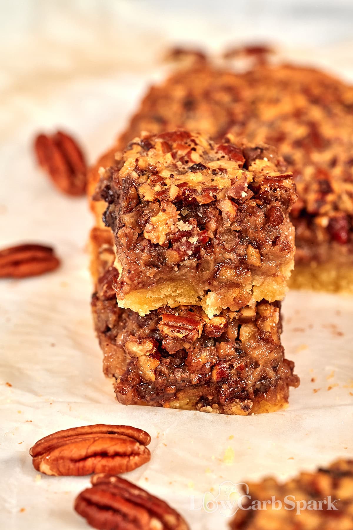 Stacked keto pecan pie bars with whole pecans scattered around them