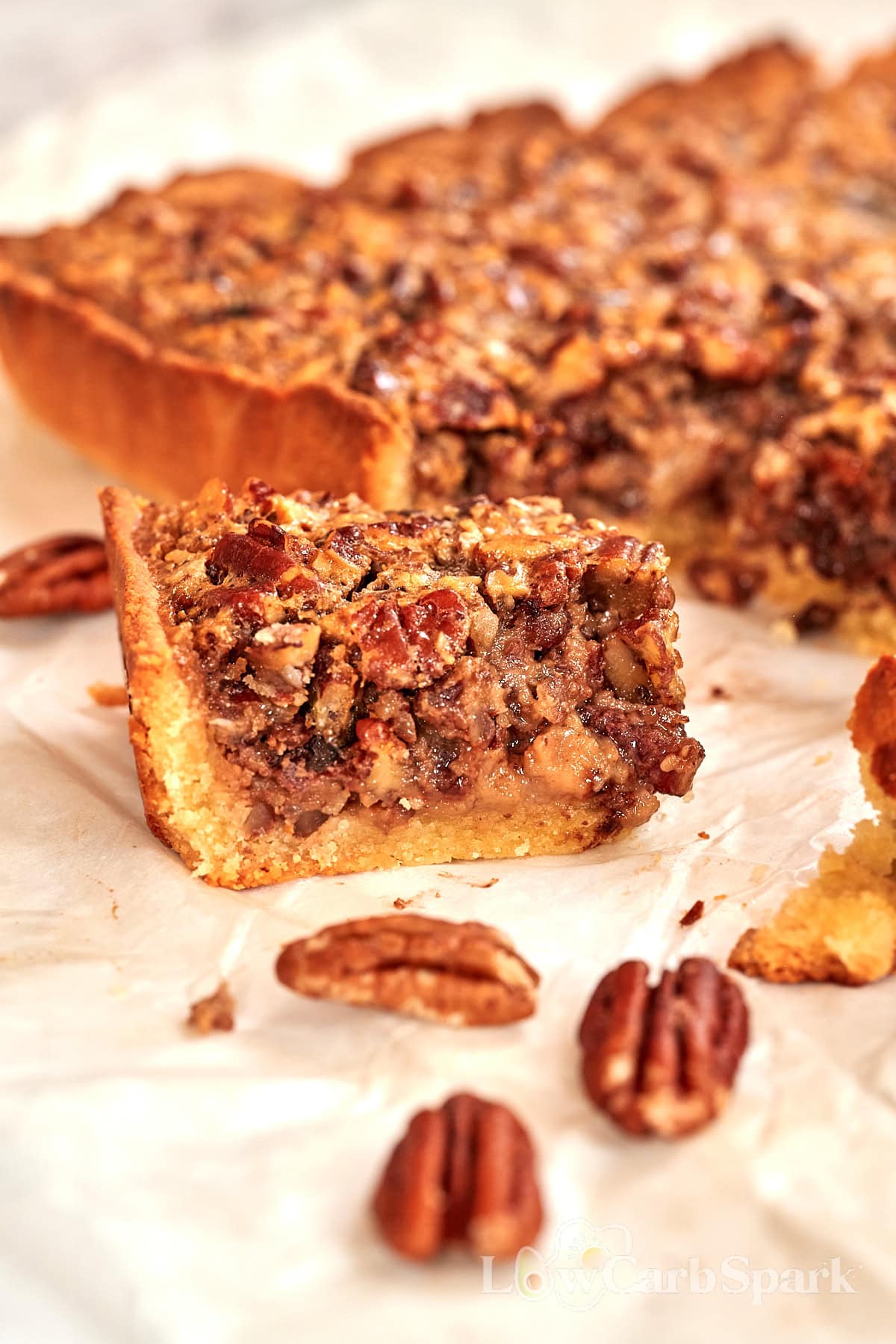 Single pecan pie bar on parchment paper, showing the filling and almond flour crust