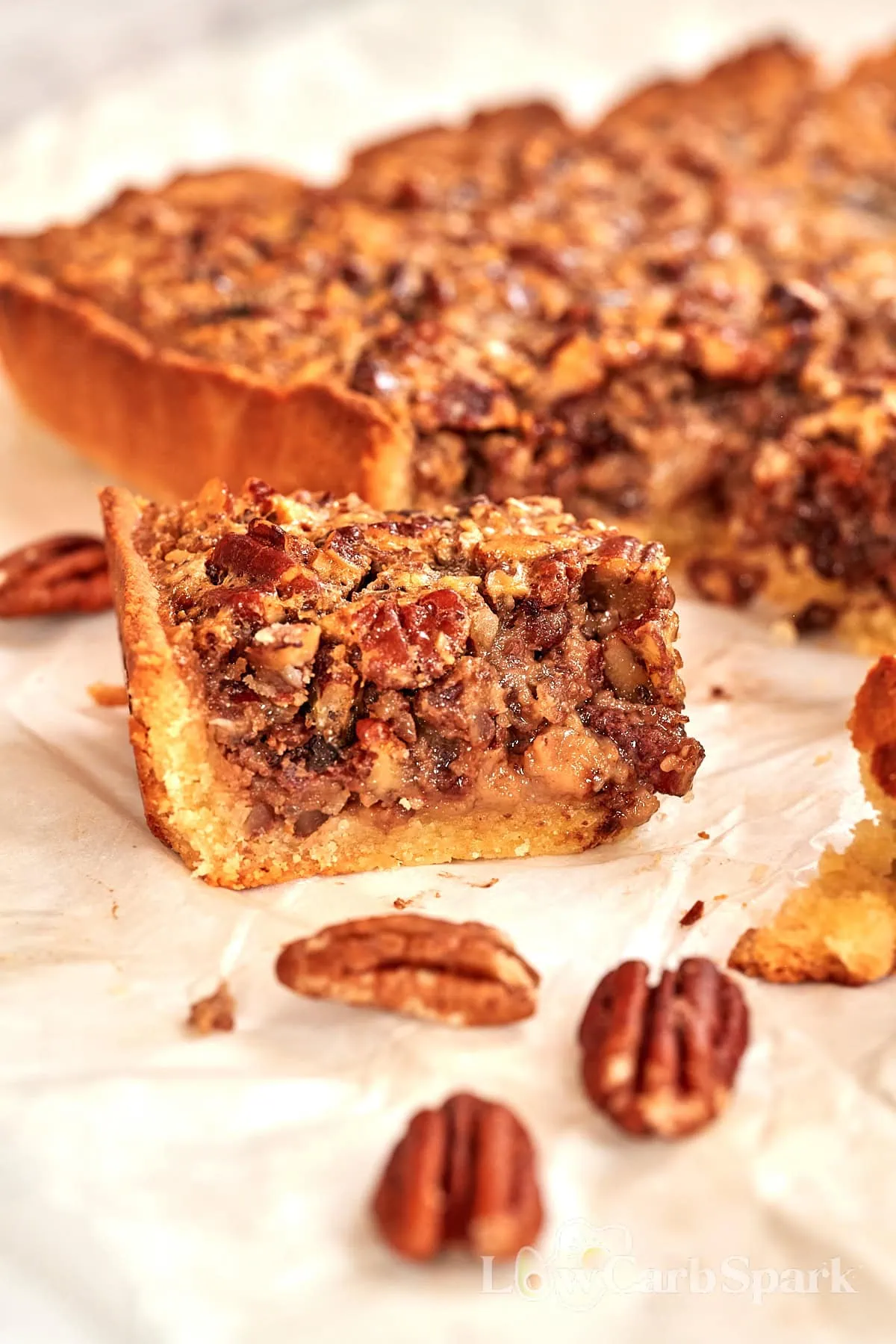 Keto Pecan Pie Bars 12 Single pecan pie bar on parchment paper, showing the filling and almond flour crust