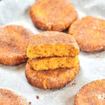 Stack of pumpkin snickerdoodle cookies coated in cinnamon with one cookie cut open