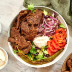 Healthy viral doner kebab bowl topped with shaved seasoned meat, crunchy vegetables, pickled onions, and a keto-friendly garlic sauce.