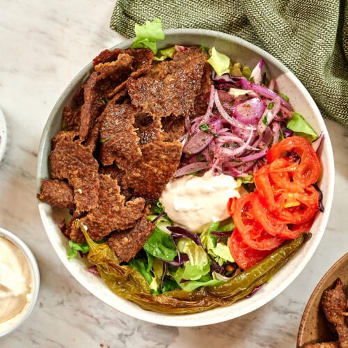 Healthy viral doner kebab bowl topped with shaved seasoned meat, crunchy vegetables, pickled onions, and a keto-friendly garlic sauce.