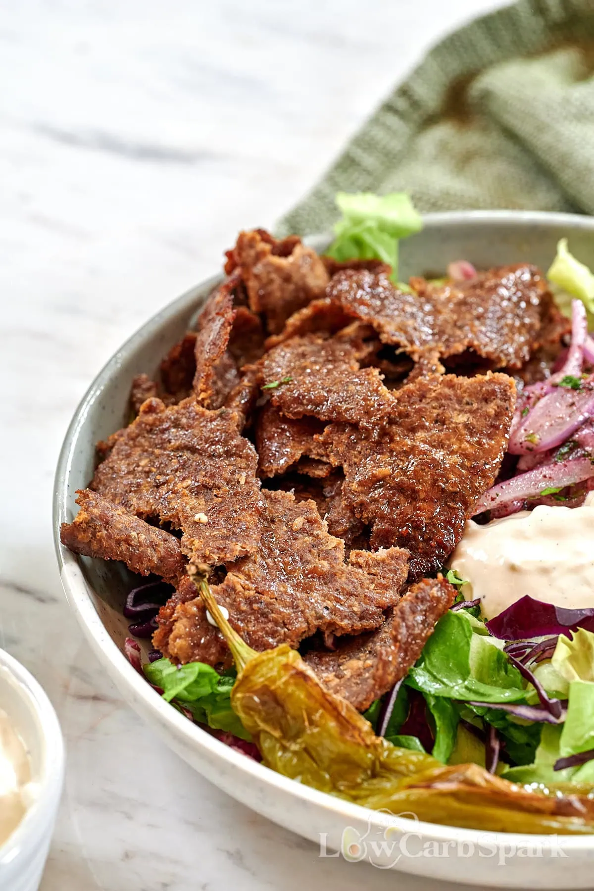 Viral Doner Kebab 2 Bowl of doner kebab featuring thin, crispy meat slices on greens with sumac onions and creamy sauce.