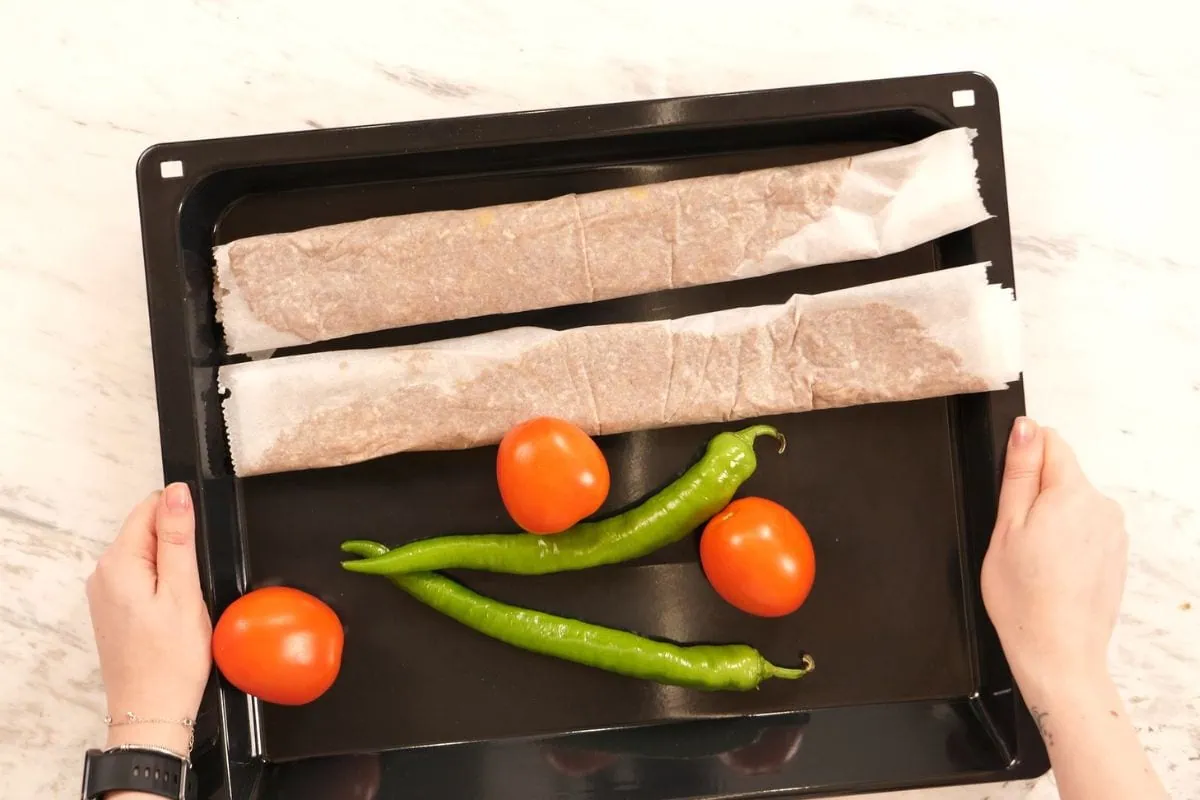 Viral Doner Kebab 8 Two parchment-wrapped kebab meat logs placed on a baking tray with tomatoes and green peppers.