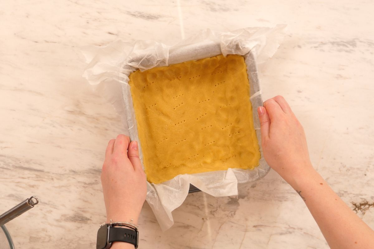 Keto pecan pie bar crust pressed evenly into a parchment-lined square baking pan and pricked with a fork.