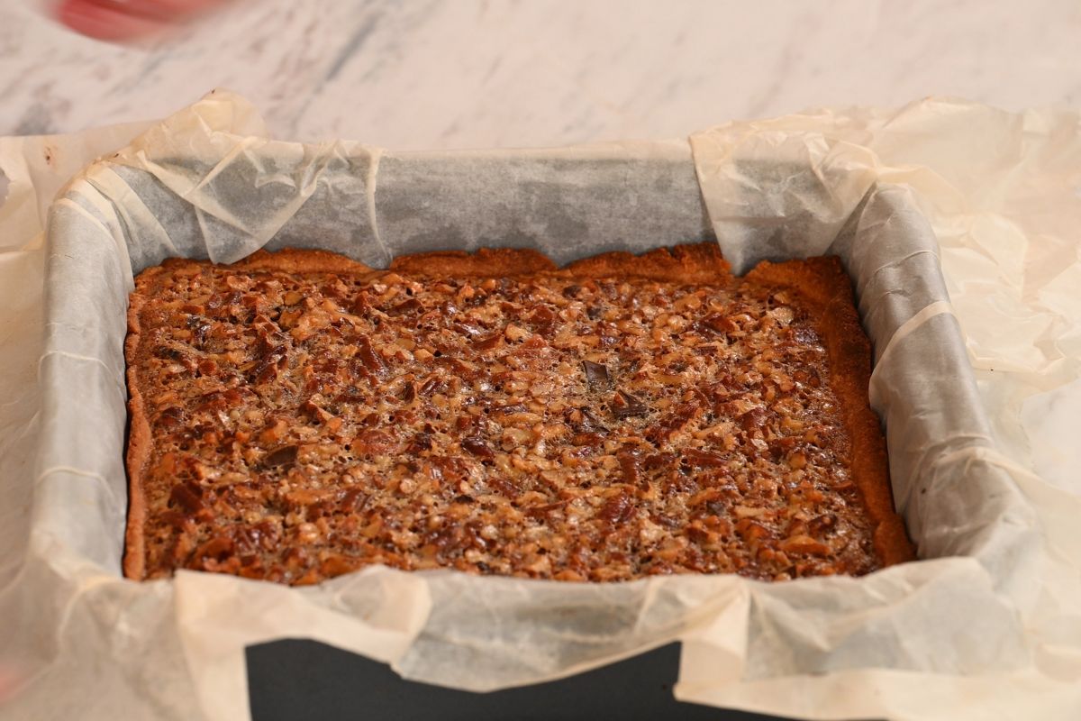 Freshly baked keto pecan pie bars in a parchment-lined square baking pan.