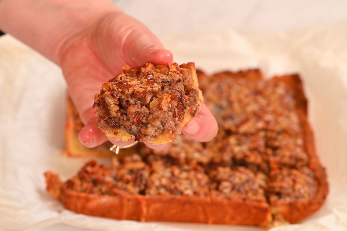 Keto pecan pie bar held in hand showing the thick gooey pecan topping and baked crust.