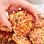 Cheesy chicken fritter held by hand, golden and crispy