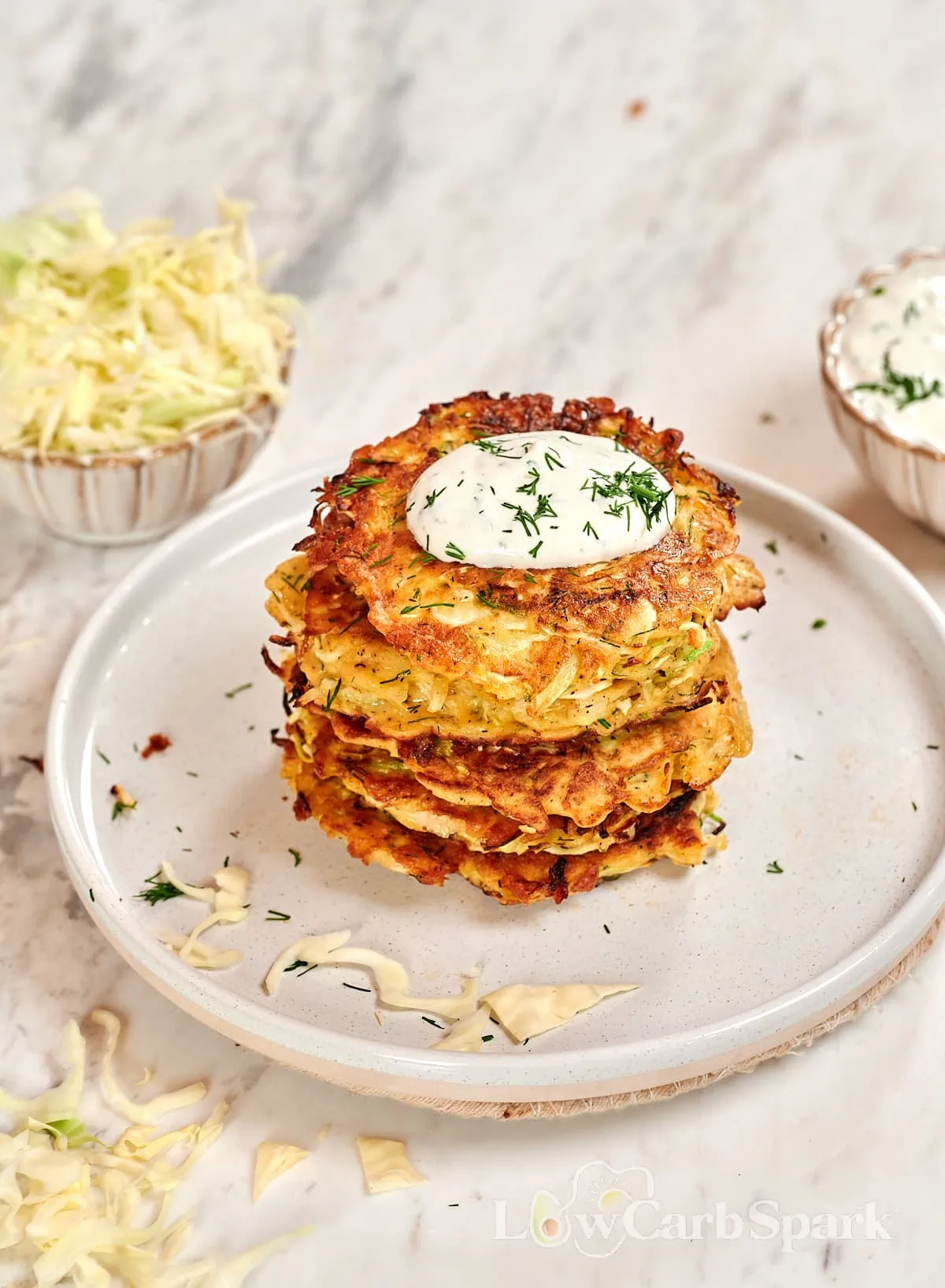 Cabbage Fritters 7 Stack of crispy cabbage fritters topped with sour cream and fresh dill on a white plate.