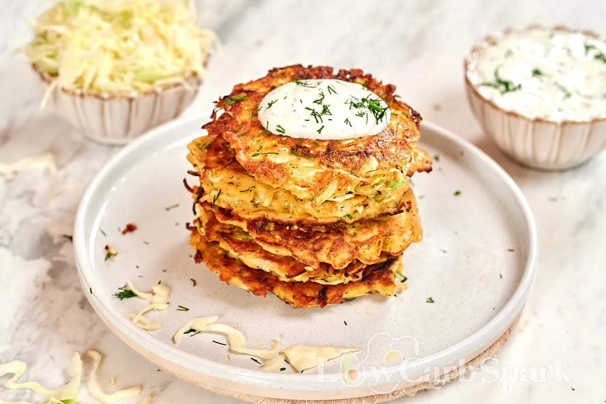 Cabbage Fritters 8 Close-up stack of golden brown cabbage fritters garnished with creamy yogurt sauce and chopped dill.