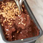 Close-up of a scoop of chocolate coconut milk ice cream with chopped nuts being lifted from the pan.