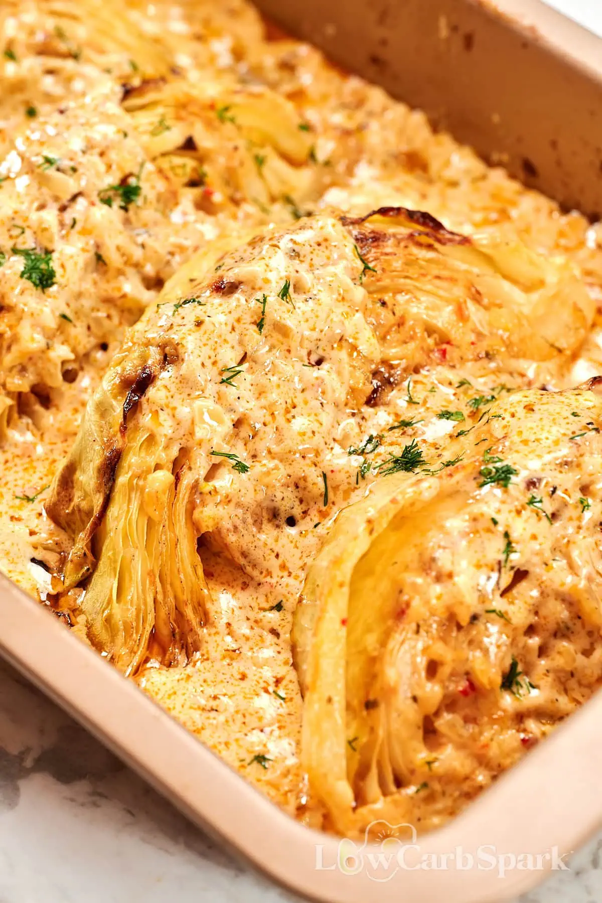 Creamy Garlic Butter Melting Cabbage 1 Creamy baked cabbage wedges in a casserole dish topped with garlic parmesan sauce and fresh herbs.