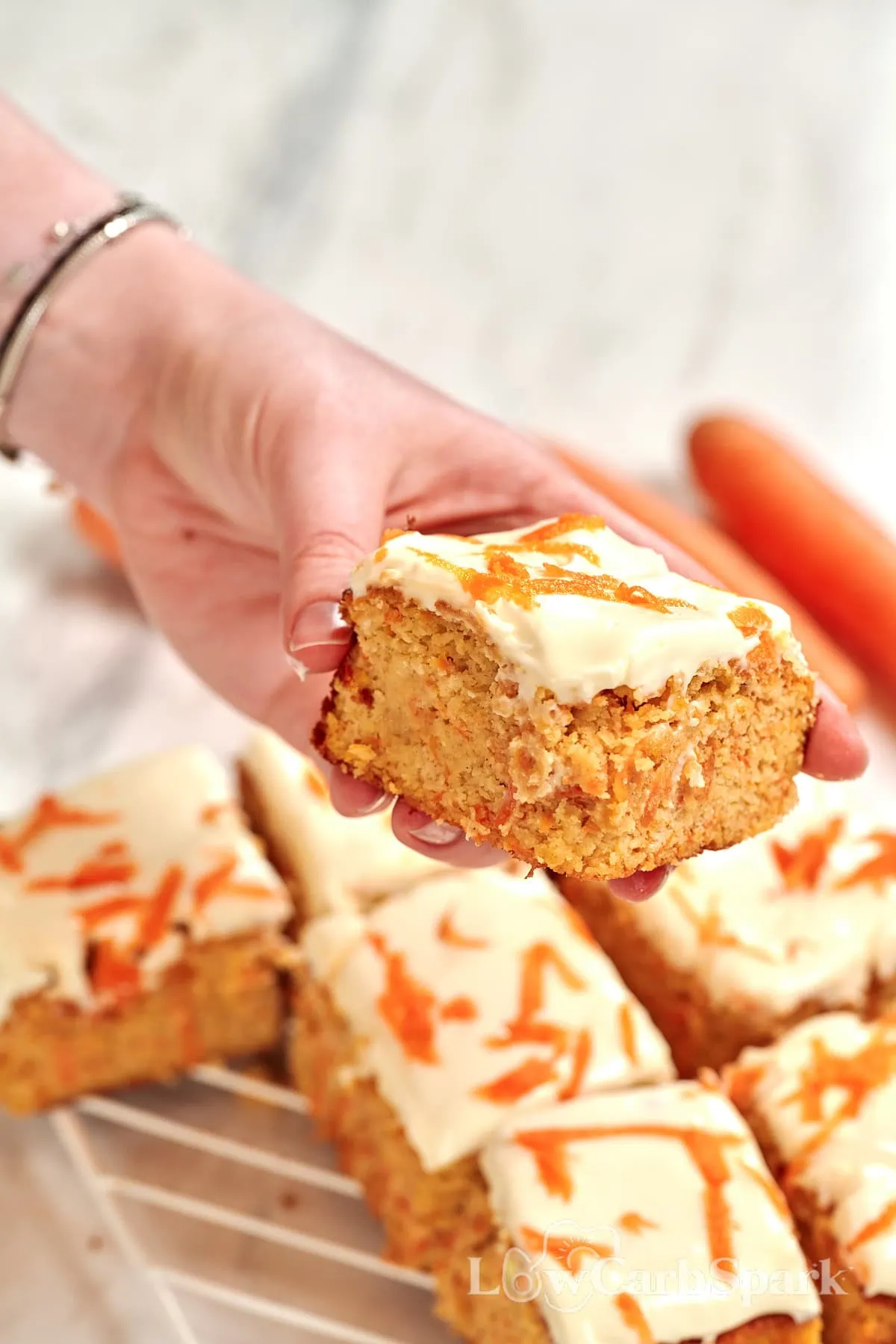 Cottage Cheese Carrot Cake Bars 2 Hand holding a square of high-protein carrot bars with creamy cottage cheese frosting.