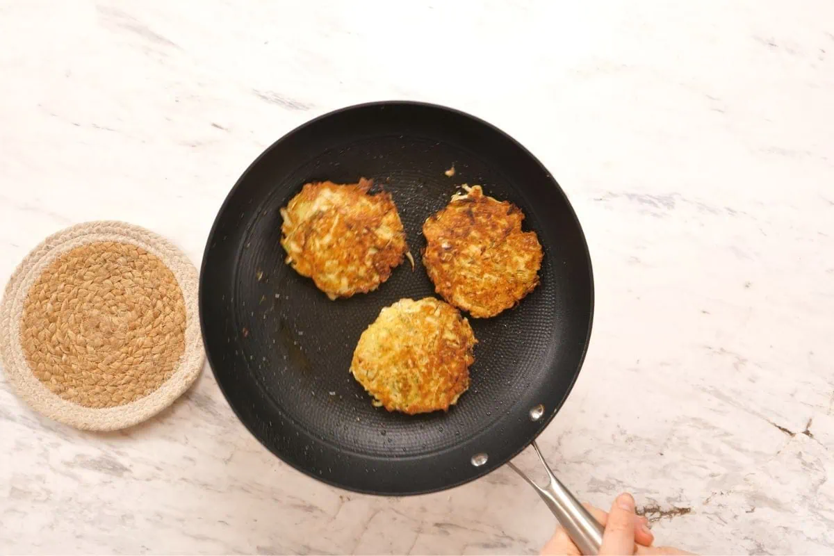 Cabbage Fritters 5 Three golden brown cabbage fritters frying in a nonstick pan until crispy.