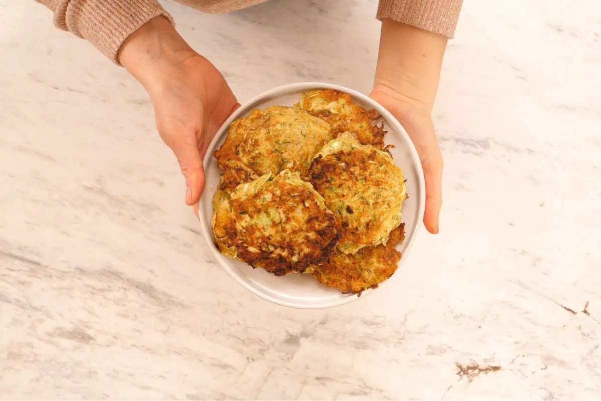 Cabbage Fritters 6 Hands holding a plate of freshly cooked crispy cabbage fritters.