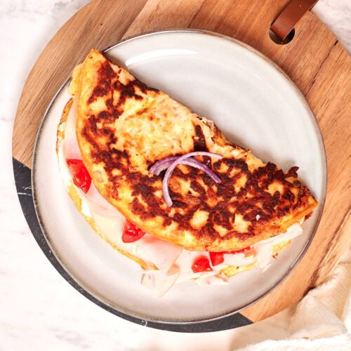Crispy halloumi egg wrap filled with turkey slices, red peppers, and onion served on a plate