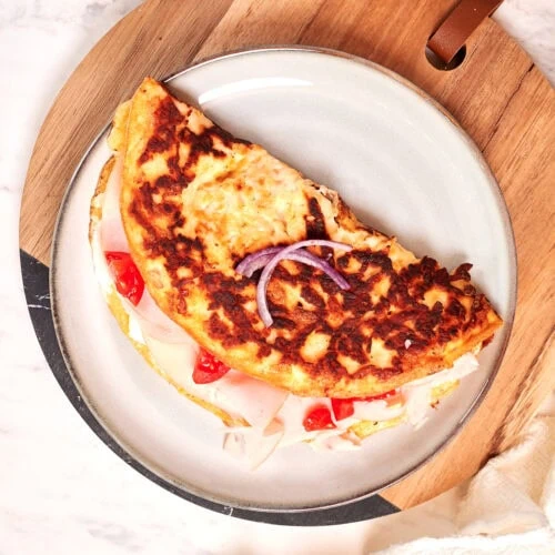 Crispy Halloumi Egg Wrap (High Protein, Low Carb) 10 Crispy halloumi egg wrap filled with turkey slices, red peppers, and onion served on a plate
