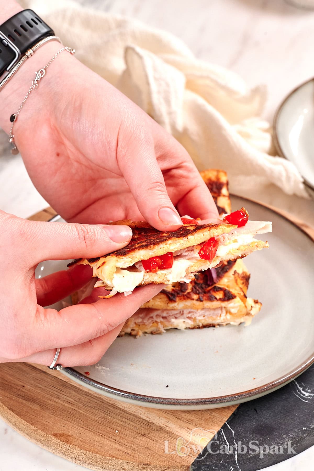 Hands holding a crispy halloumi egg wrap with melted cheese, turkey, and fresh vegetables inside
