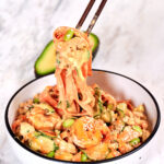 Chopsticks lifting sushi roll salad with shrimp, cucumber ribbons, edamame, and creamy spicy sauce