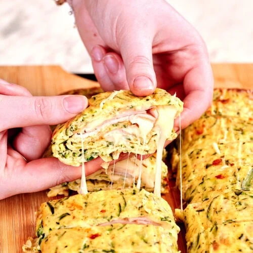 Zucchini Ham and Cheese Roll 2 Hands pulling apart a zucchini ham and cheese roll with melted cheese stretching between the slices.