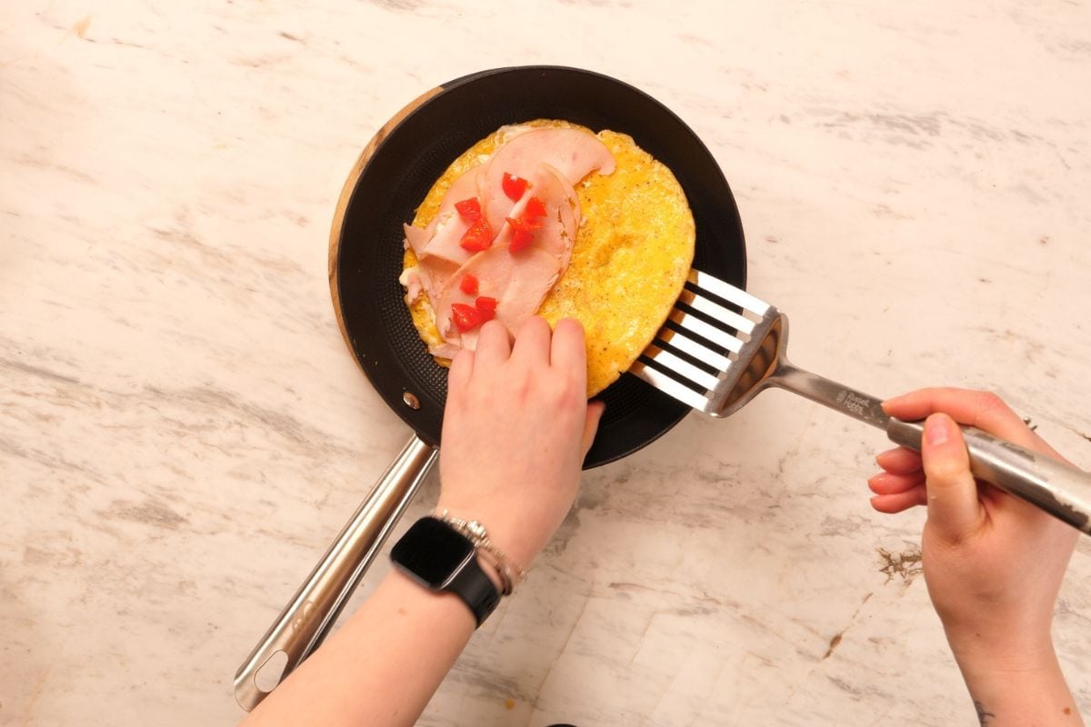 Adding ham and toppings to halloumi egg wrap in skillet