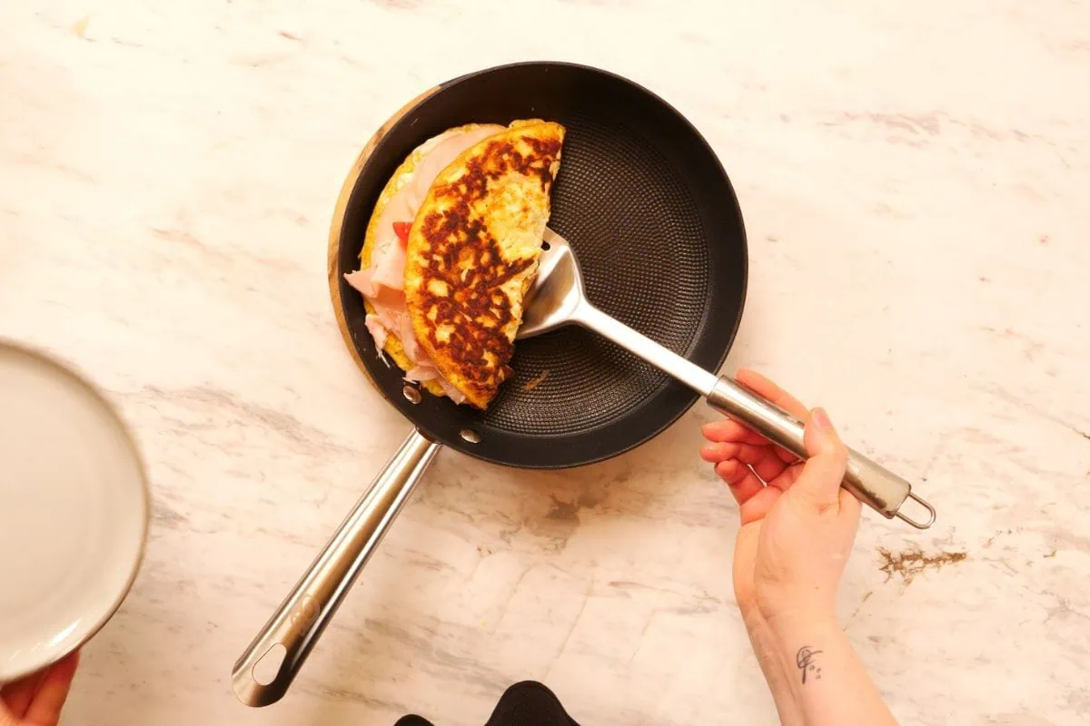 Crispy Halloumi Egg Wrap (High Protein, Low Carb) 8 Folding crispy halloumi egg wrap with ham and cheese filling
Lifting folded egg wrap from pan with spatula