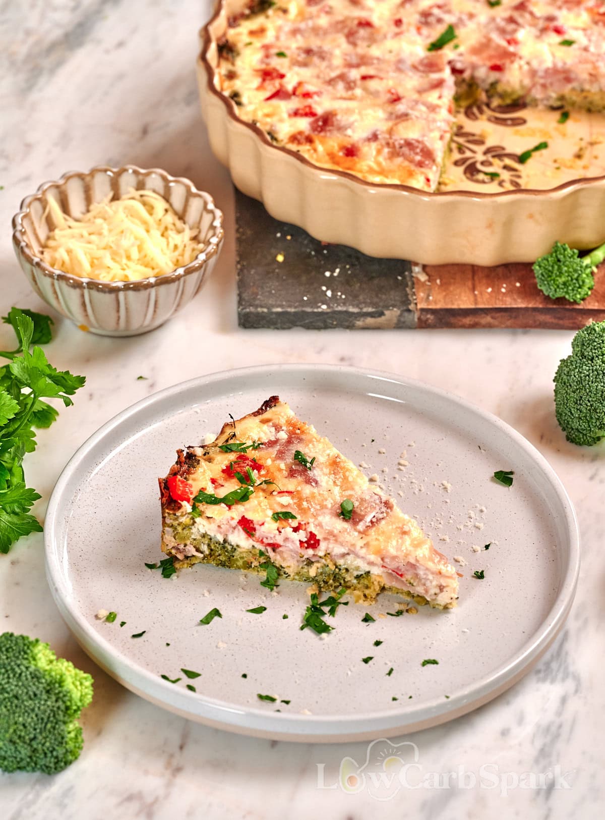 Cheesy Broccoli Crust Quiche 1 Slice of cheesy broccoli crust quiche with ham, broccoli, and cheese served on a white plate.