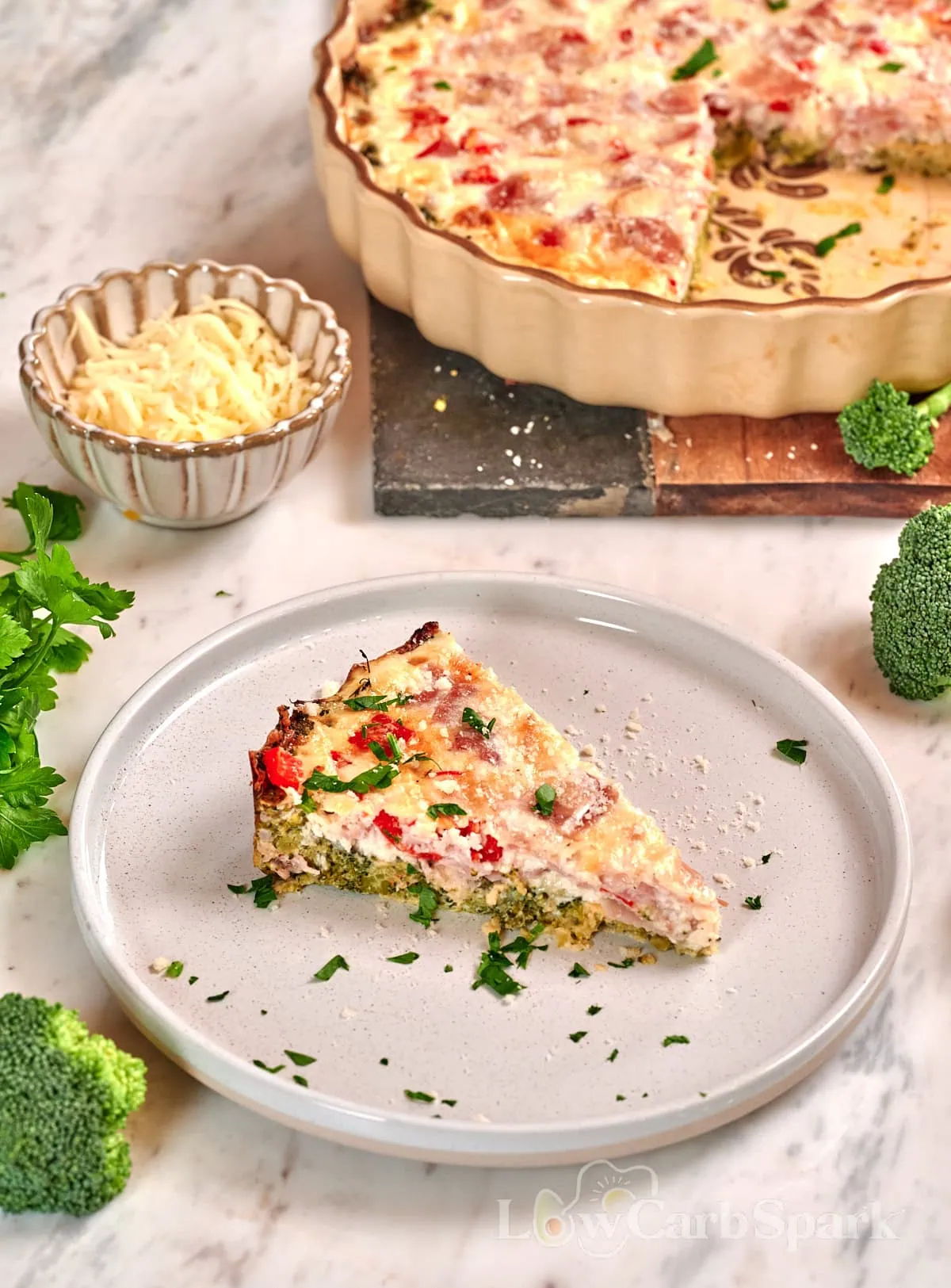 Cheesy Broccoli Crust Quiche 1 Slice of cheesy broccoli crust quiche with ham, broccoli, and cheese served on a white plate.