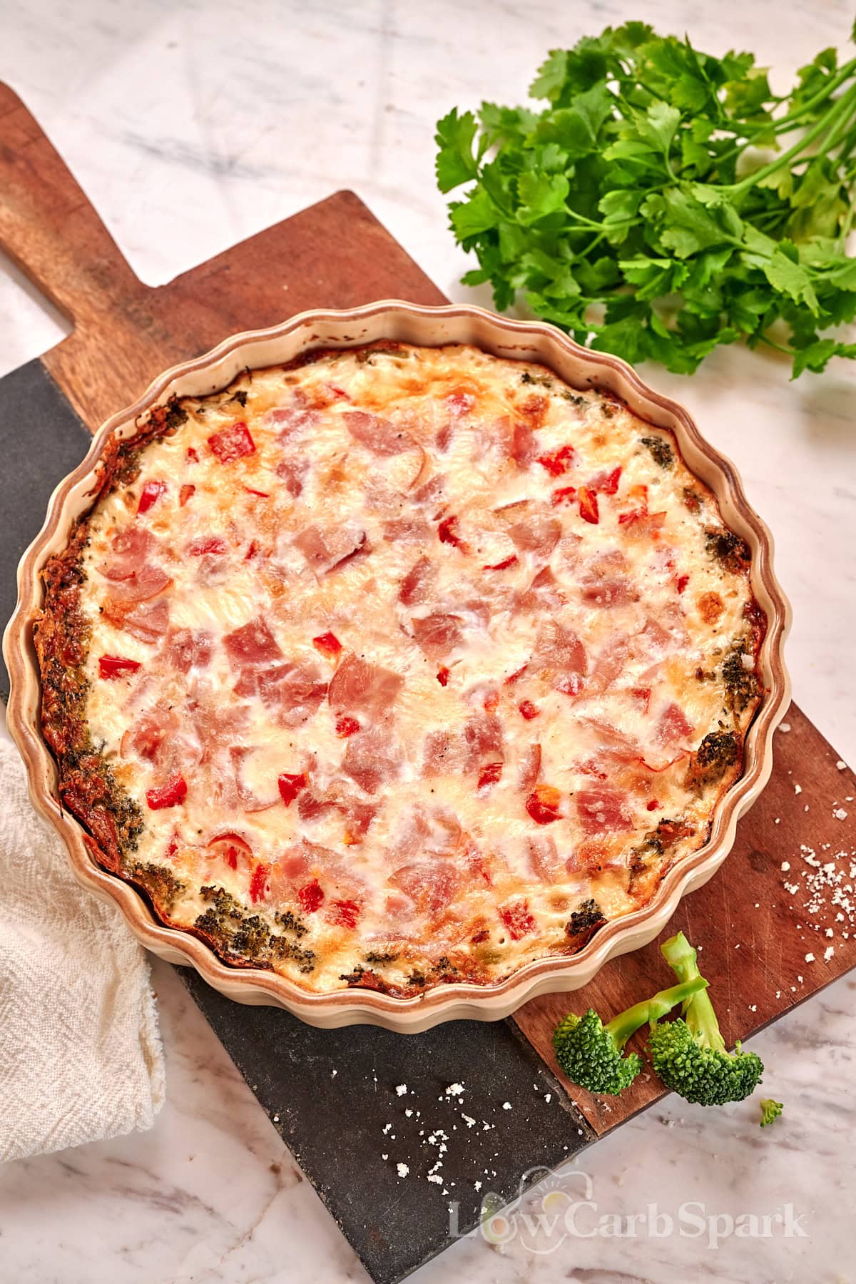 Cheesy Broccoli Crust Quiche 2 Overhead view of baked cheesy broccoli crust quiche topped with ham and red peppers in a tart pan.