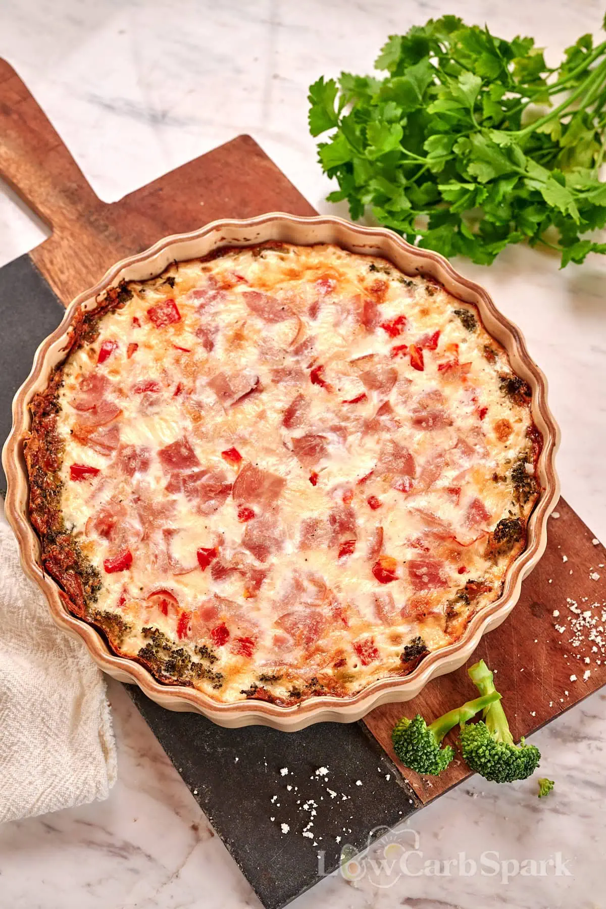 Cheesy Broccoli Crust Quiche 2 Overhead view of baked cheesy broccoli crust quiche topped with ham and red peppers in a tart pan.