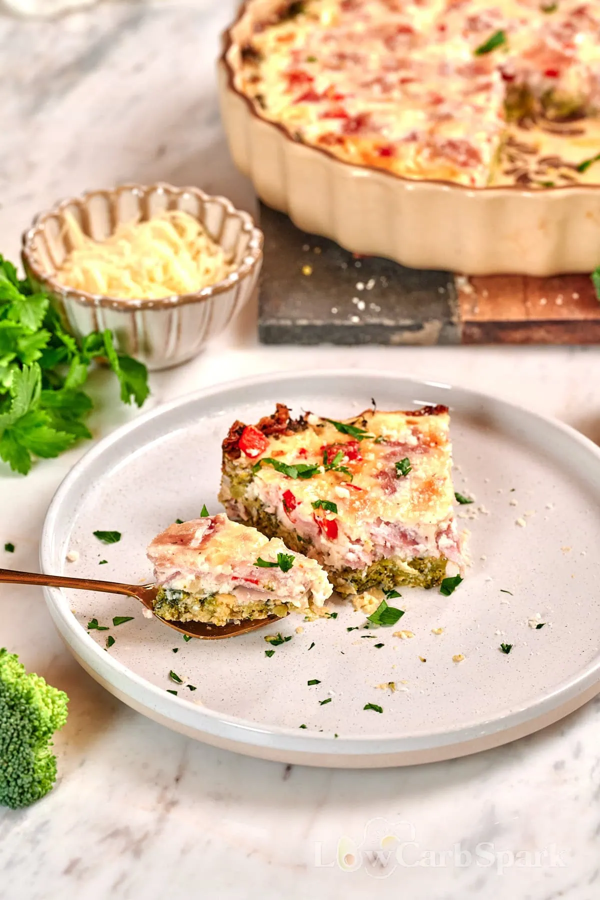 Cheesy Broccoli Crust Quiche 9 Bite of cheesy broccoli crust quiche on a fork with the remaining slice plated in the background.