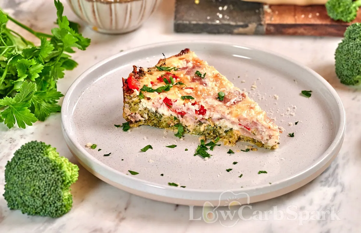 Cheesy Broccoli Crust Quiche 10 Slice of cheesy broccoli crust quiche with ham, broccoli, and cheese served on a white plate.