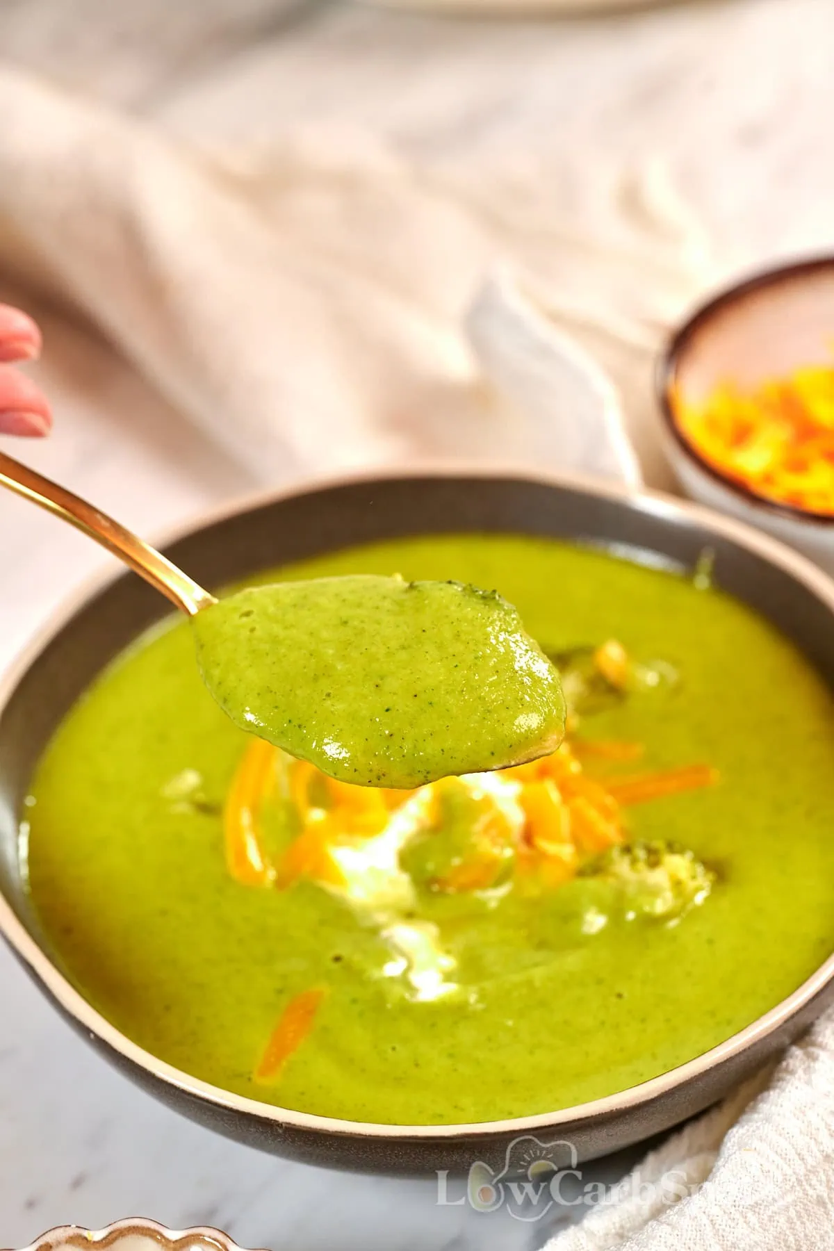 High-Protein Broccoli Soup (Creamy & Easy) 11 Spoonful of creamy high-protein broccoli soup with cheddar cheese topping served in a bowl.