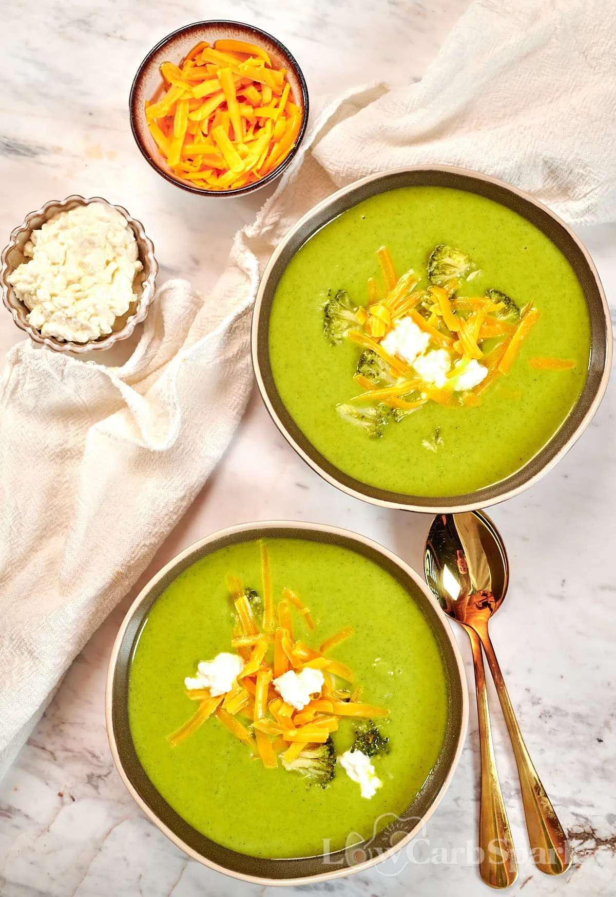 High-Protein Broccoli Soup (Creamy & Easy) 12 Two bowls of creamy high-protein broccoli soup topped with cheddar cheese, cottage cheese, and broccoli florets.